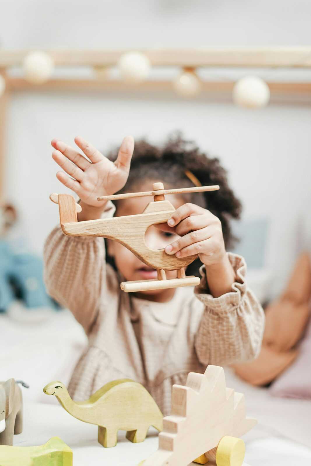 Child playing with a wooden helicopter toy indoors, enjoying imaginative play.