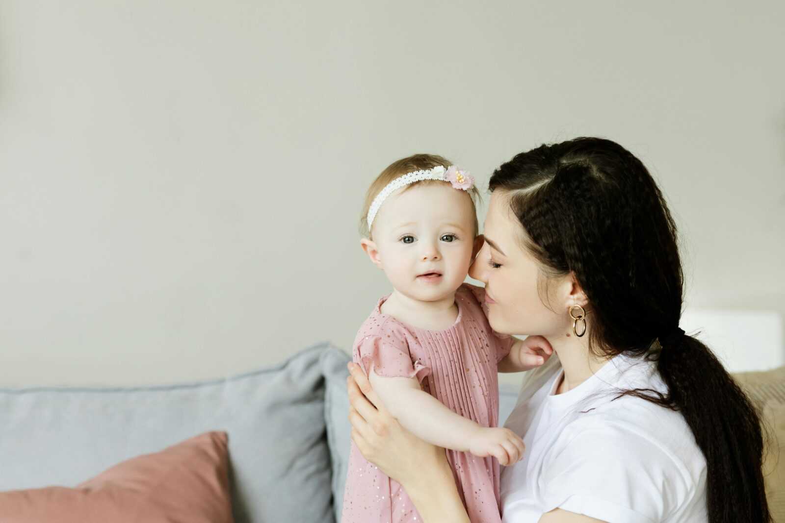 Tender moment of a mother kissing her baby daughter. Warm and loving family scene indoors.