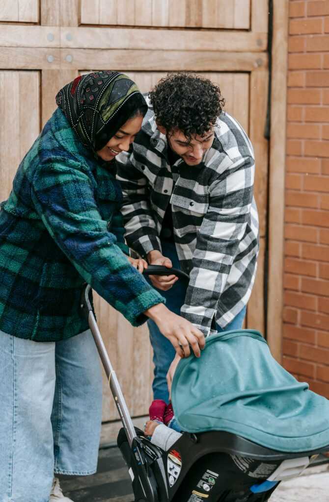Positive African American mother and father standing near baby sitting in baby carriage on street in city near building